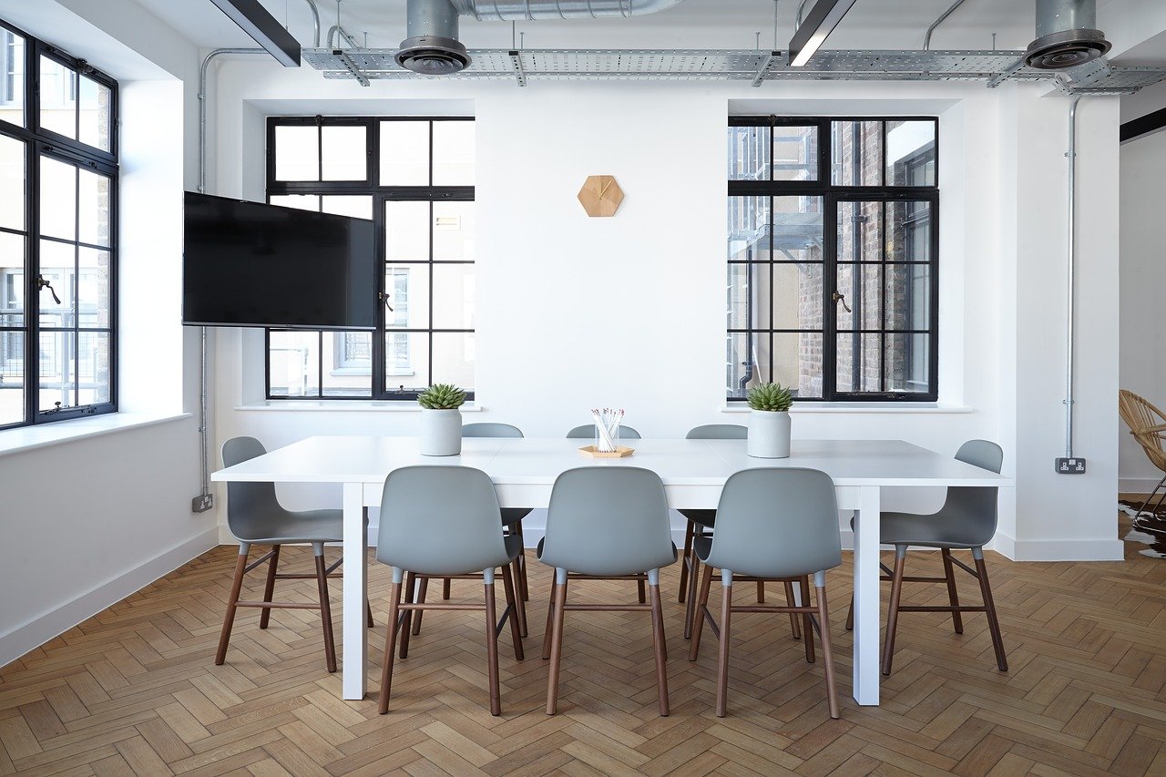 Sala de trabalho com mesa branca e oito cadeiras.