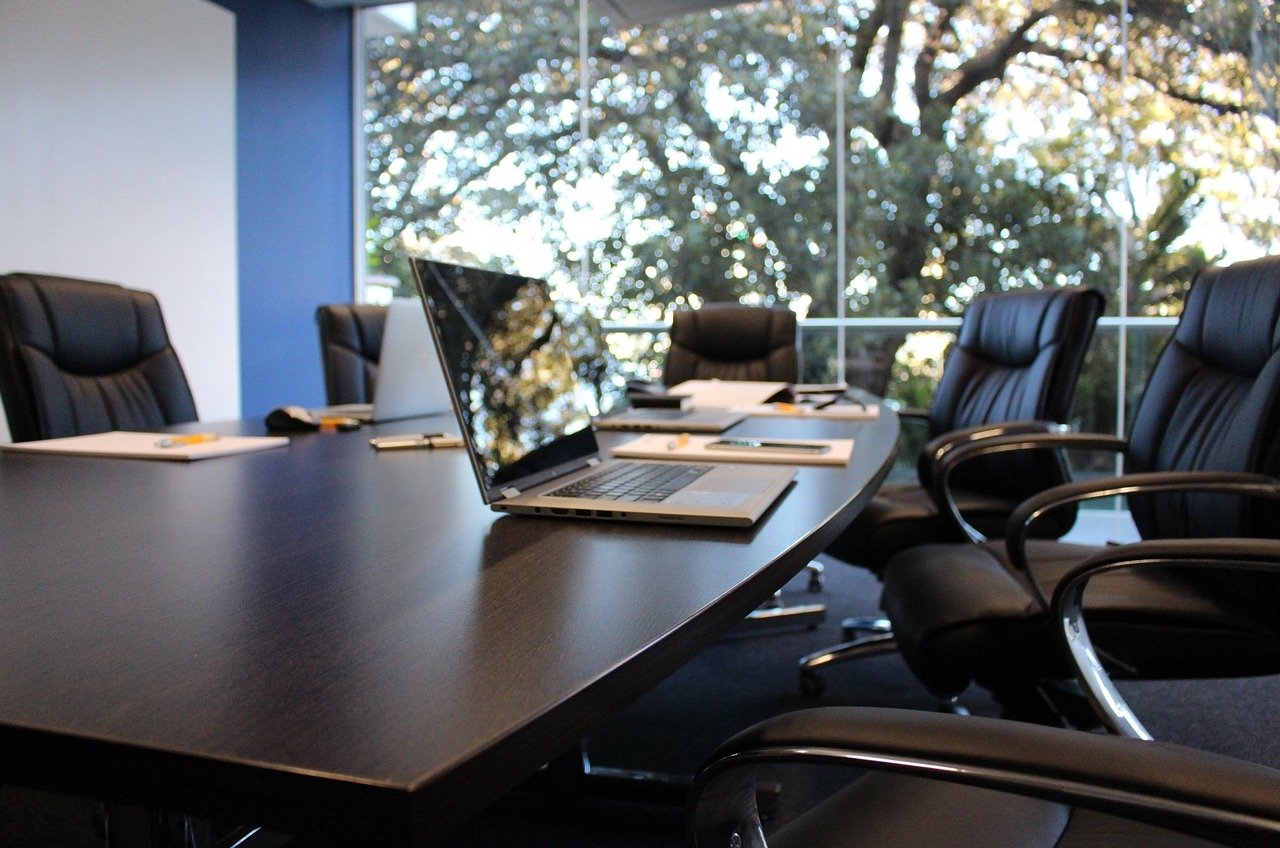 Sala de reunião com cadeiras de couro e um notebook sob a mesa.